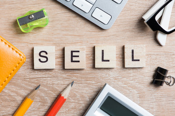 Office stuff and SELL word spelled with wooden blocks on workplace table