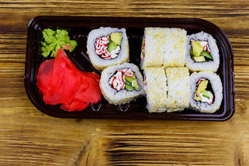 Uramaki sushi rolls with surimi in plastic box on wooden table. Top view. Sushi for take away or delivery of sushi in plastic container
