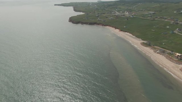 Aerial tilt reveal view of village on green Magdalen Islands coast in daylight