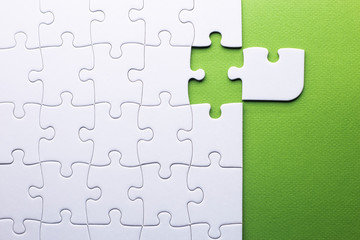 white puzzle with piece that does not fit on a green background