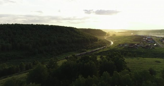 Passenger train an electric locomotive under the rock near river by two-sided winding Trans Siberian railway in the Ural Mountains - Aerial Photography, drone wide view at summer sunny day