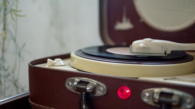 A vinyl disc on a player, record player spinning vinyl disk. Old-fashioned retro player with a disk on it, pan shot close up of music played on a brown vinyl turntable