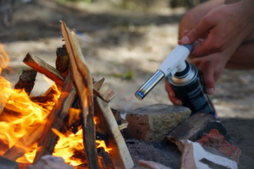 Hand holds manul gas burner near firewood