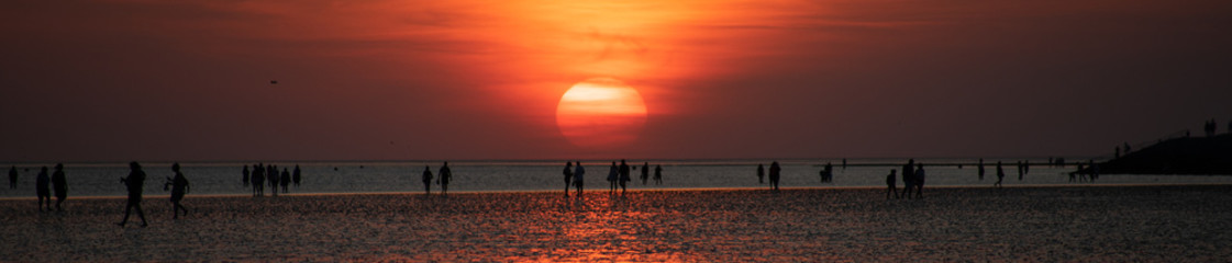 Panorama of People on the beach in the sunset off Buesum in the Wadden Sea.
