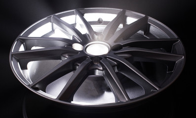 Modern beautiful car alloy wheel in the form of rays that is highlighted by rays of light and sparkle, black background
