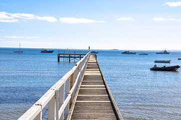 Obraz premium One point perspective view toward the sea with ships sailing and wooden bridge in the middle during the summer period.