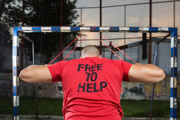 A man in a red t-shirt trains outside using a red resistance band.