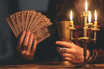 Fortune teller with deck of tarot cards in the light of burning table.