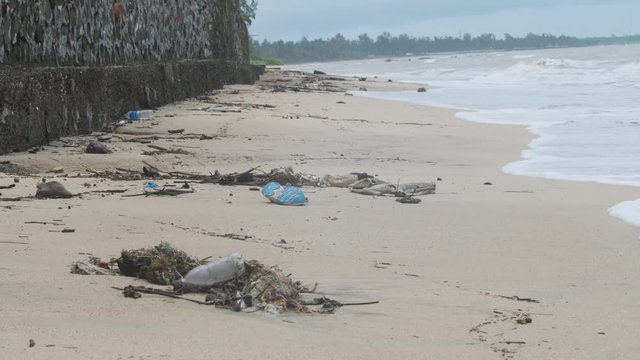 Waves washing up on a sand beach covered in plastic trash garbage rubbish debris wide