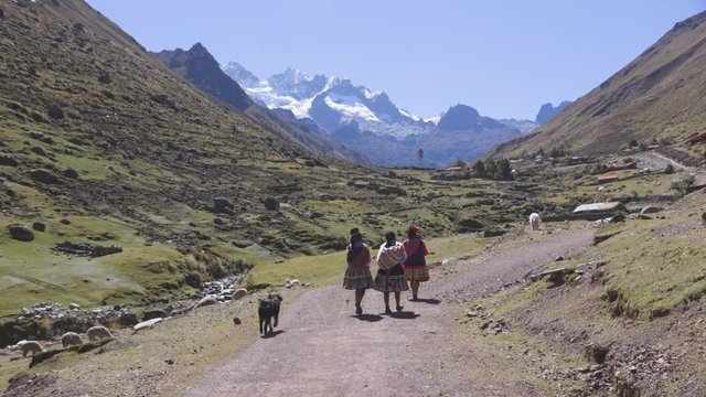 A group of Quechuan woman walking along a dirt road towards a mountain in a remote village in the Peruvian Andes.