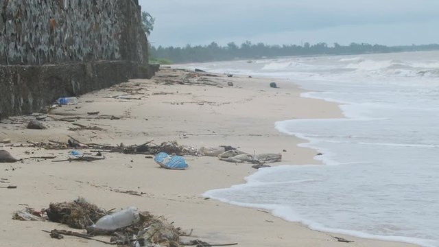 Waves washing up on a sand beach covered in plastic trash garbage rubbish debris slow motion wide
