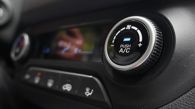 Close-up of pushing a button to turn on the air conditioner in a car. The mans hand turns the button
