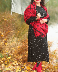 Attractive mature plus size woman in a stylish black dress with polka dots and a red plaid scarf with an umbrella walking near the lake on a foggy autumn day.Woman's life after 40
