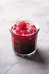 Fresh ice cold fruit cocktail in glass, refreshing summer red currant berry drink on stone concrete background, angle view