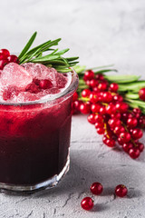 Fresh ice cold fruit cocktail in glass, refreshing summer red currant berry drink with rosemary leaf on stone concrete background, angle view
