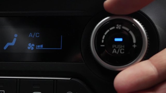 Close-up of pushing a button to turn on the air conditioner in a car. The mans hand turns the button and adjusts the comfort in the car