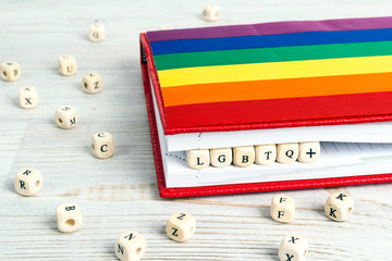 LGBTQ+ written in wooden blocks in red notebook with rainbow LGBT flag on wooden table.