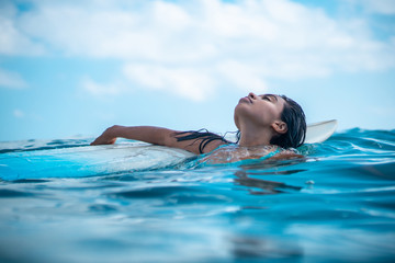 Portrait of surfer girl on white surf board in blue ocean pictured from the water in Bali