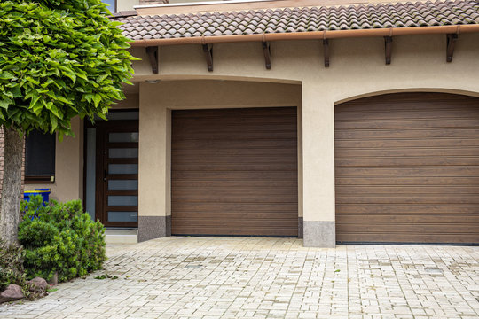 Brick stone driveway double garage doors with green tree. Elegant brown house driveway

