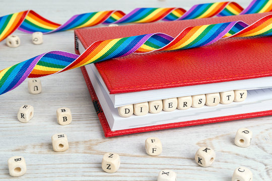 Word Diversity written in wooden blocks in red notebook with rainbow LGBT ribbon on wooden table.