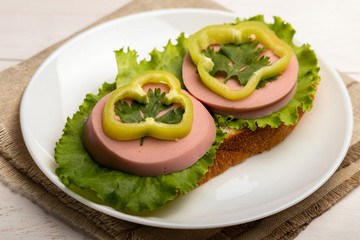 sandwich with sausage, lettuce and paprika rings