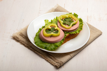 sandwich with sausage, lettuce and paprika rings