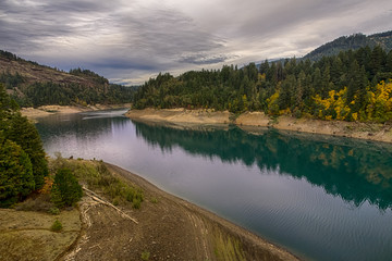 Fototapeta premium Beautiful autumn river landscape in South Oregon, USA. Moody sky and vivid colors foliage reflect in calm river water