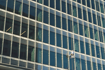 Fototapeta na wymiar Guy washing the windows od this high rise as he eases himself down.