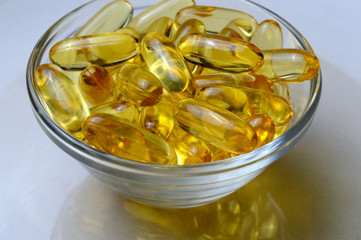 Omega-3 and Vitamin D fish oil capsules in a glass plate.