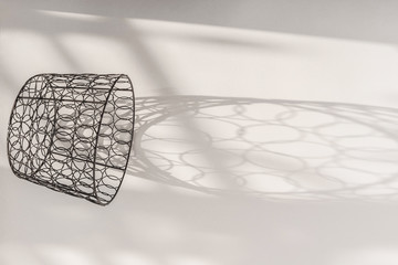 Decorative metal basket and long shadows from it on a white table.