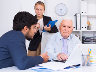 Mature male is talking to colleague, while the secretary writing important information.