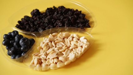 Berries ad nuts in round plastic container for food storage - yellow background