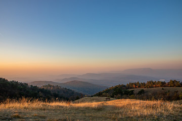 A separate bench in between the hills of Nagy-Szénás mountain in Hungary, misty view on the forests, just before sunset