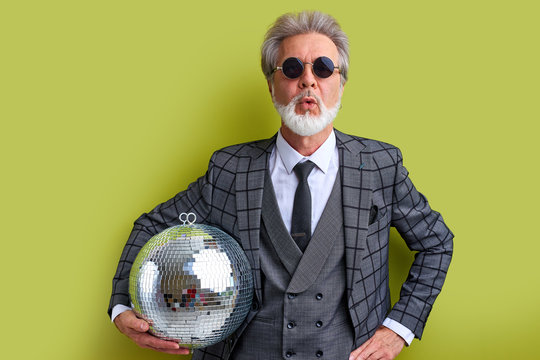 shocked senior man going to celebrate, dance and have fun. surprised emotional man in formal wear hold disco ball and look at camer isolated over green background