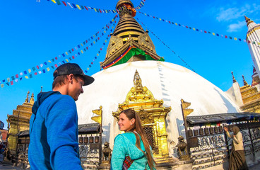 Couple walking into the boudhanath Temple in Kathmandu, Nepal. Many colourful prayer flags with 'om...