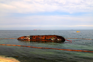 An old rusty tanker flooded and lies in Odessa, Ukraine. Oil spills from the ship and pollutes the sea water. Environmental pollution, water resources, environmental disaster.