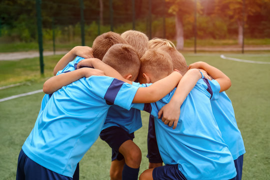 Kids football team embrace each other on football field before match outdoors at summer