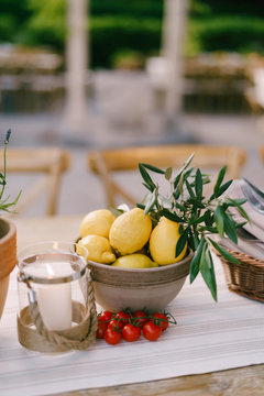 Deep plate with lemons on the table with a sprig of cherry tomatoes on a blurred background.