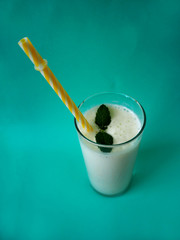 milk banana cocktail with a sprig of mint in a glass with a yellow tube on a turquoise background