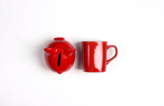Red Piggy Bank And Red Coffee Mug On White Background.