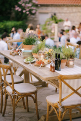 A festive table with fresh flowers in pots in a restaurant with chairs and guests on a blurred background.