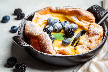 Dutch baby pancake with berries and lemon in cast iron frying pan.