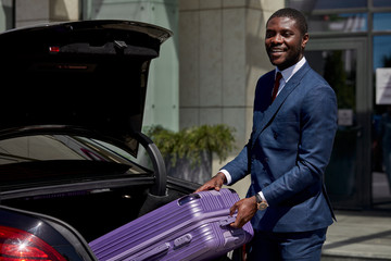 confident black transfer carry suitcases of clients in luxurious car, private tranfer enjoy working with business people