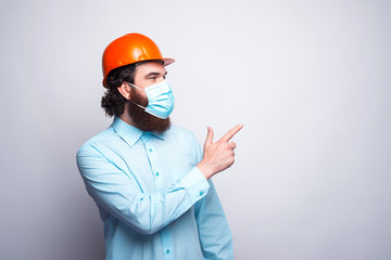Portrait of young worker architect wearing medicinal mask and pointing away.
