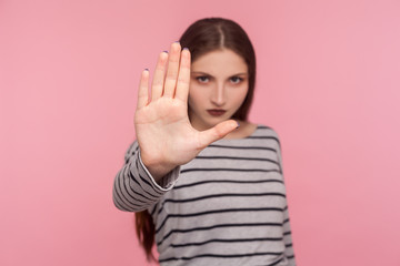Portrait of strict serious woman in striped sweatshirt showing stop to camera, warning of danger,...
