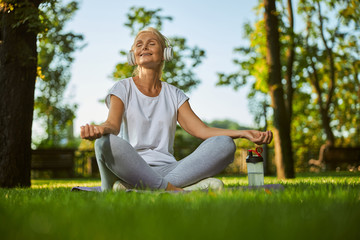 Charming woman in headphones practicing yoga in park