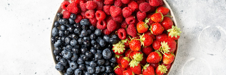 Fresh berries. Different berries in a white ceramic plate on a light table. Strawberries, raspberries and blueberries on a plate. Top view with space for text. Banner