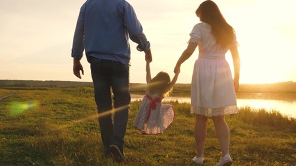 healthy baby playing with dad and mom on field in sunset light. little daughter holds mom and dad by hands and jumps on beach under yellow sun. Walking child in nature. happy, healthy family concept.
