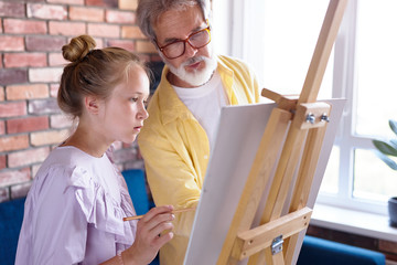 personal art teacher teach little girl to draw on easel, senior man and student girl painting...