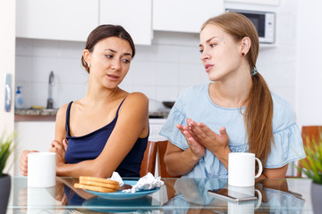 Obraz na płótnie Canvas Regretful girl begging forgive to her annoyed friend in kitchen